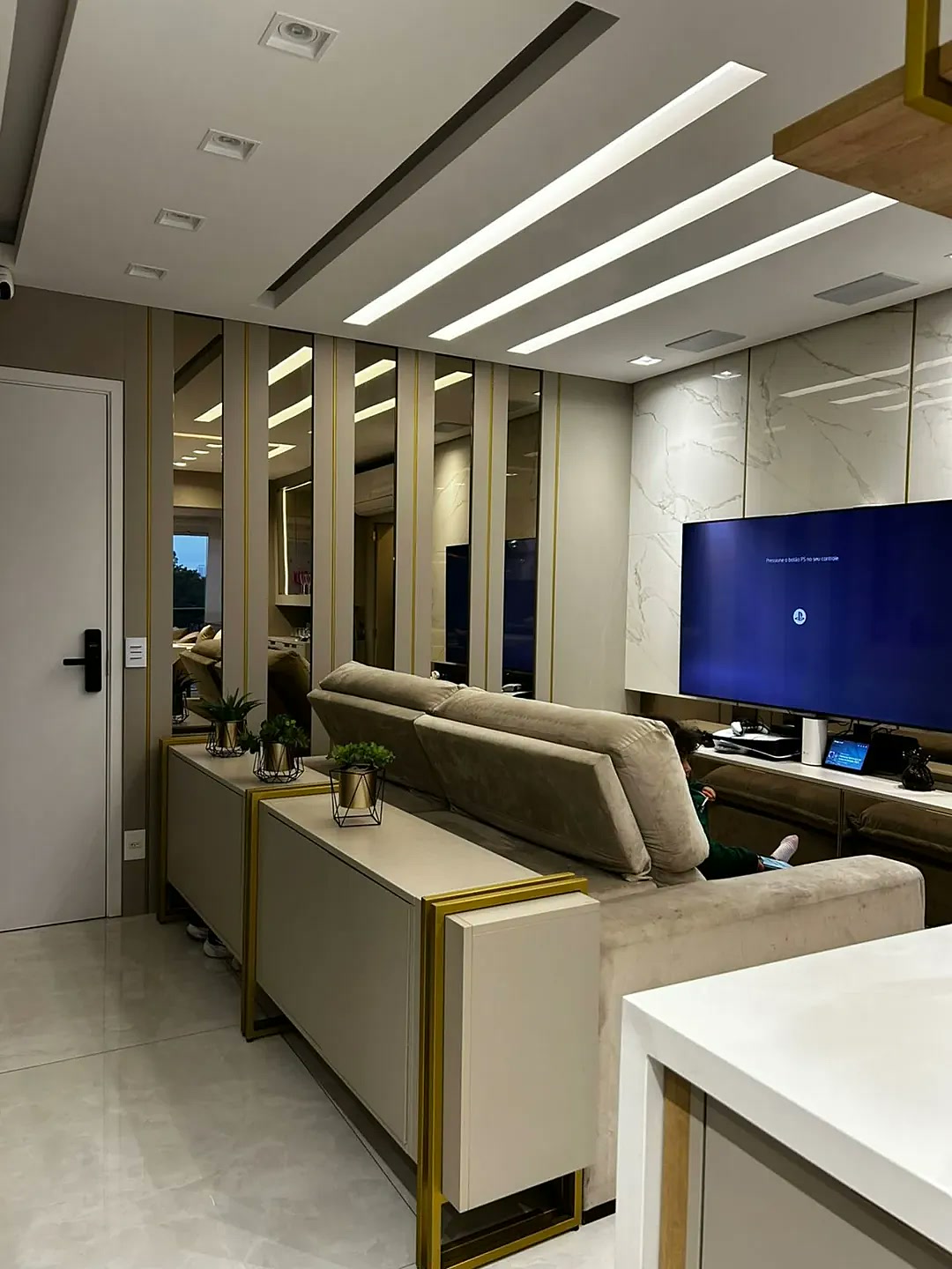 Sala de estar planejada com painel de espelhos dourados, revestimento em mármore e iluminação LED no teto – showroom Estillo Design Av. do Oratório SP